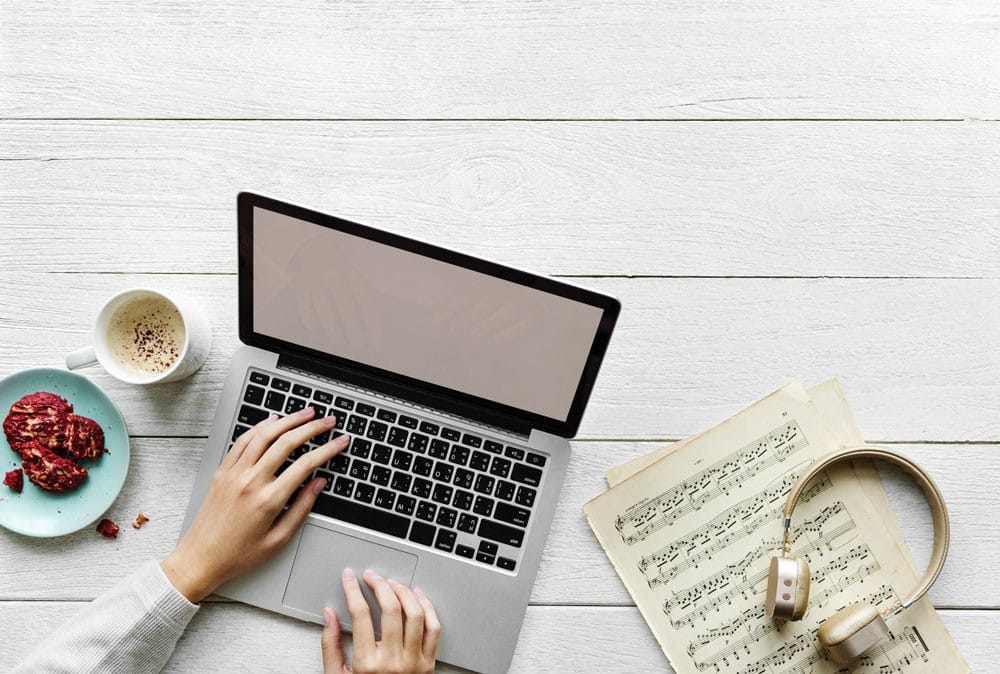 Enchufe Australia mesa de madera en la que una persona está escribiendo en un ordenador portátil Apple, partituras de música, un café y unas galletas de frambuesa